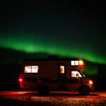 An rv parked on a field in rural Saskatchewan under the northern lights.