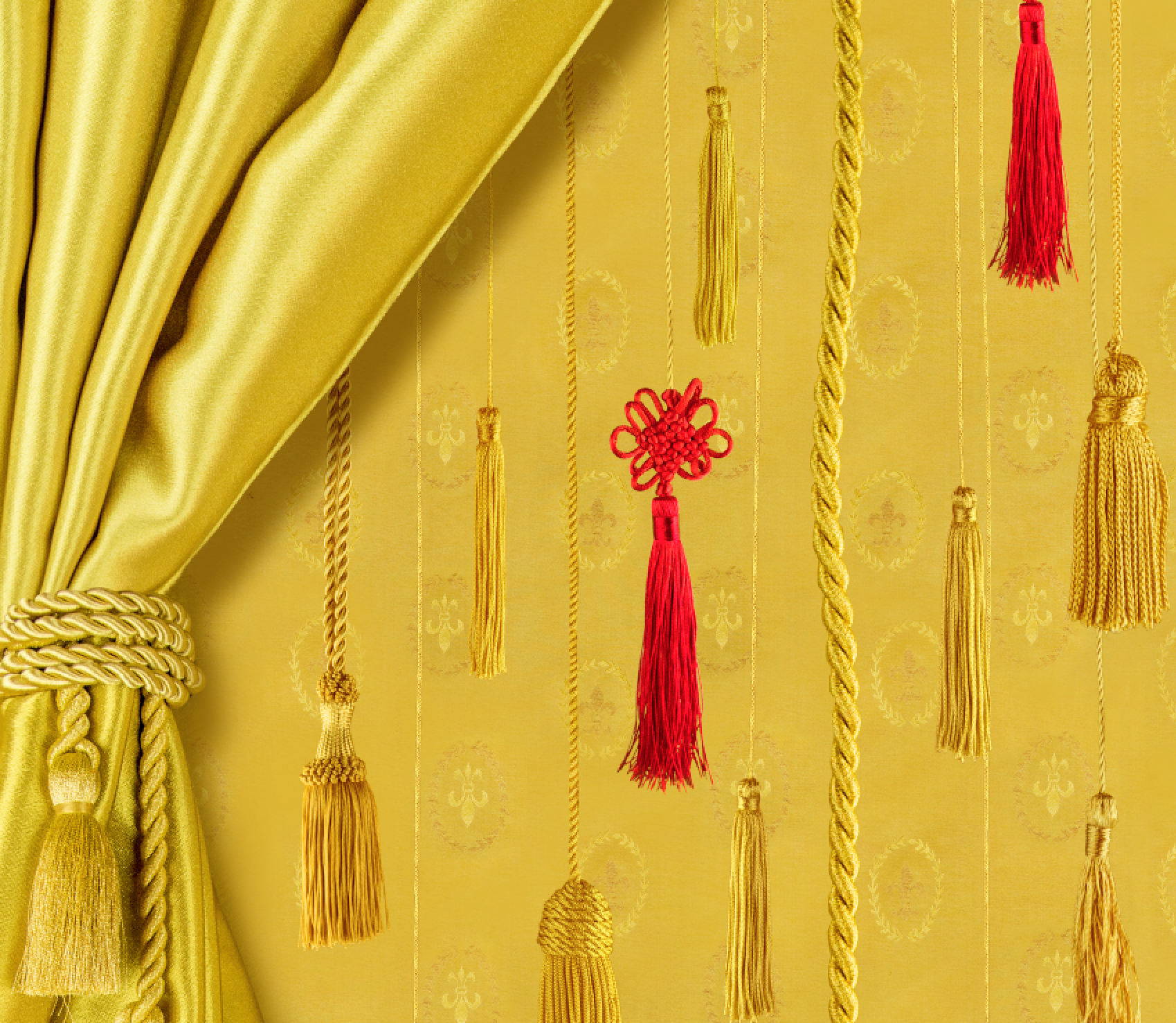 A yellow curtain is pulled to the side by a shiny, gold rope. It reveals eight gold Chinese endless knots and two red Chinese endless knots, which are made from the same rope that is holding the curtain to the side. They are suspended at varying depths and heights.