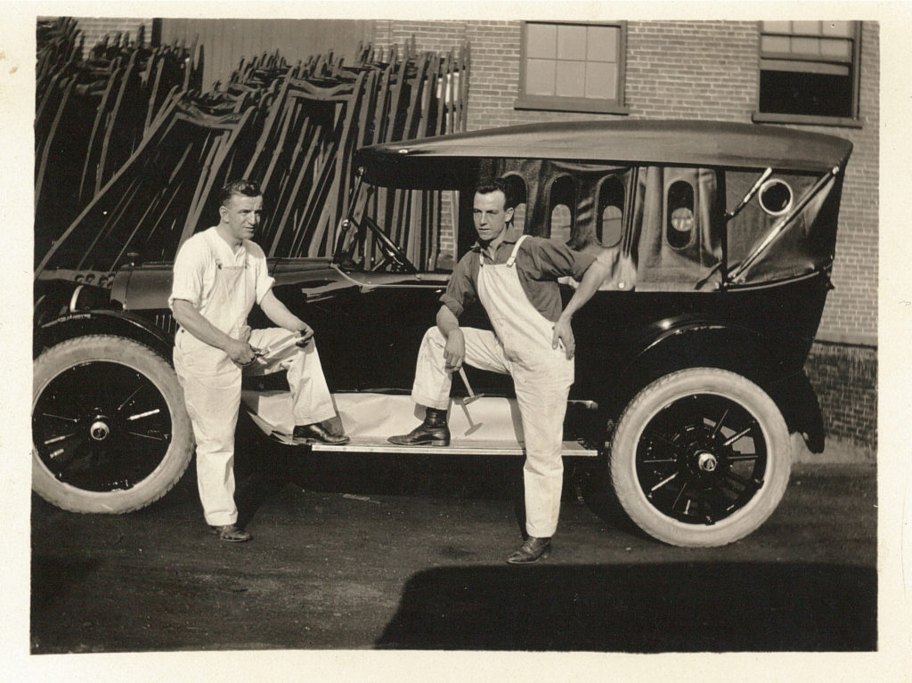 General Motors Workers, c. 1920s. Gift of Evelyn McGrath Two men stand with one foot on the ledge of a car. The men are wearing overalls and have tools in their hands.