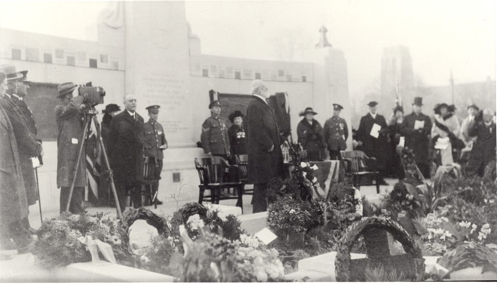 War Memorial, 1924 In the centre of this image, an older man stands in an long coat. He has white hair and a short beard. Behind him, a man in a long coat is taking a photo, using a camera that is made up of a box on a tall tripod. Around the man with white hair and the camera man, a group of people gather in a semi circle. They are dressed formally which includes top hats, fur coats, and military suits.