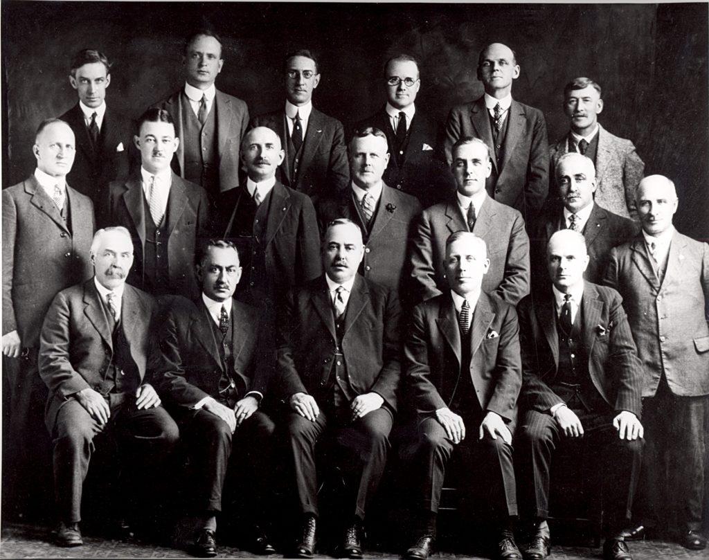 The First City Council, 1924 Three rows of men sit or stand while posed for this portrait. They are all dressed in suits.