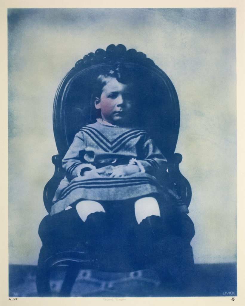 A blue cyanotype photograph of a young child sitting on a chair in front of a white wall.